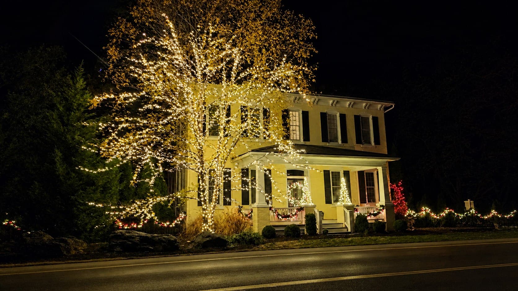 Warm-white roofline and wrapped porch column lighting on a stone home in Lititz, Pennsylvania